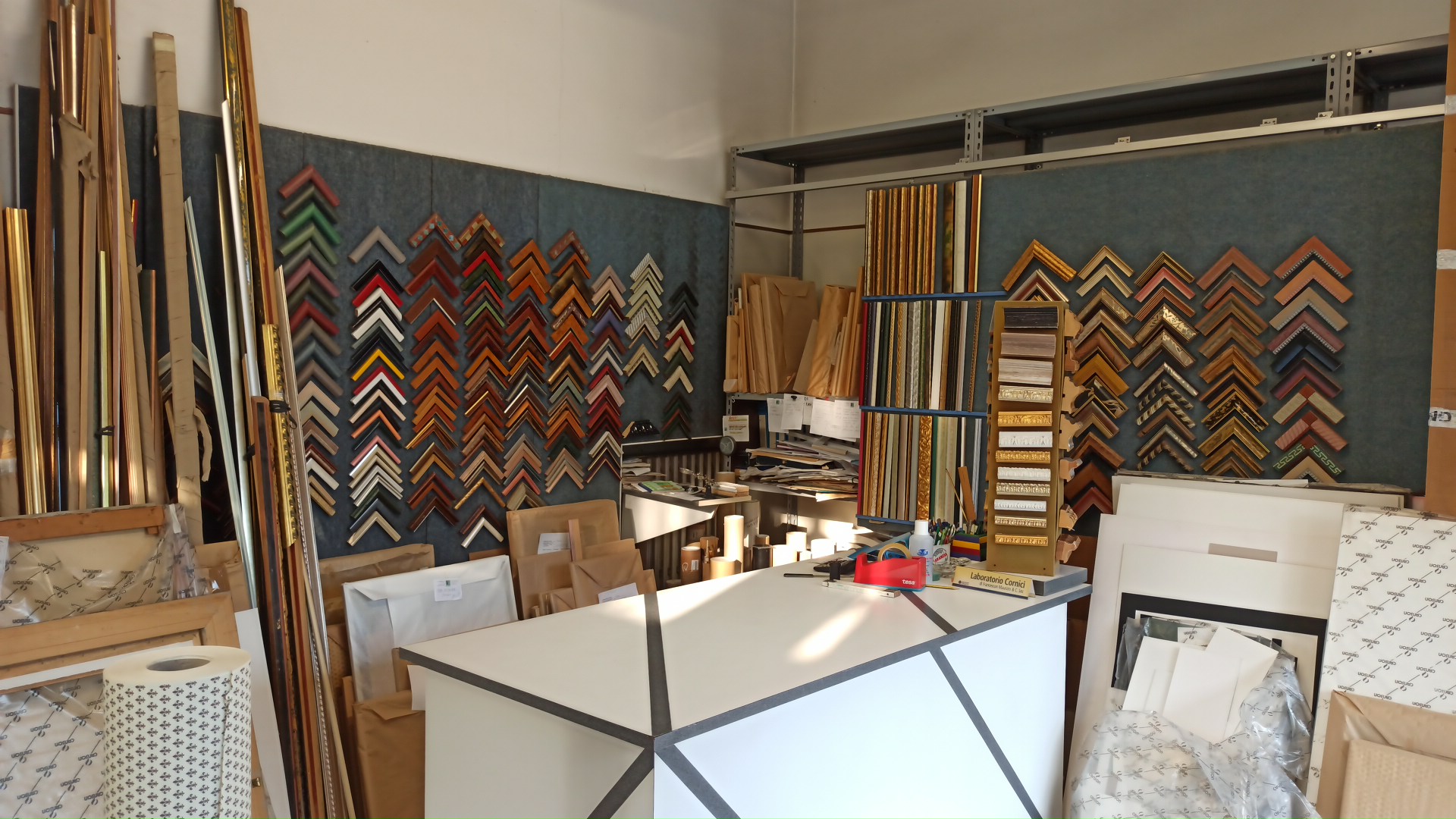 Interno dell’atelier: campioni di cornici, aste in legno e bancone di lavoro